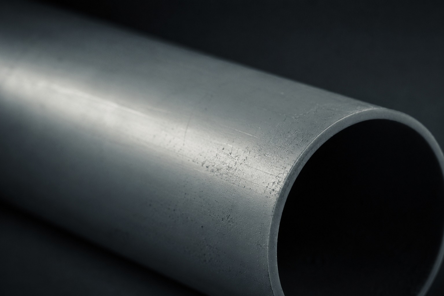 A single large-diameter pipe running diagonally through the frame in close-up, cool grey under overhead light.
