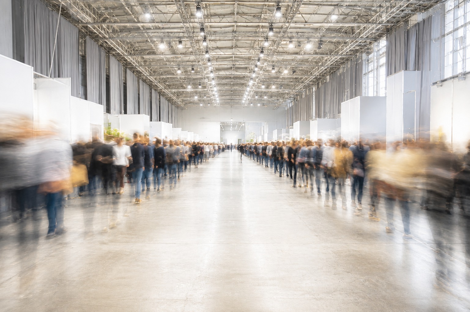 A wide hall aisle at long exposure, the crowd on either side blurred into movement while the aisle itself stays empty and sharp.